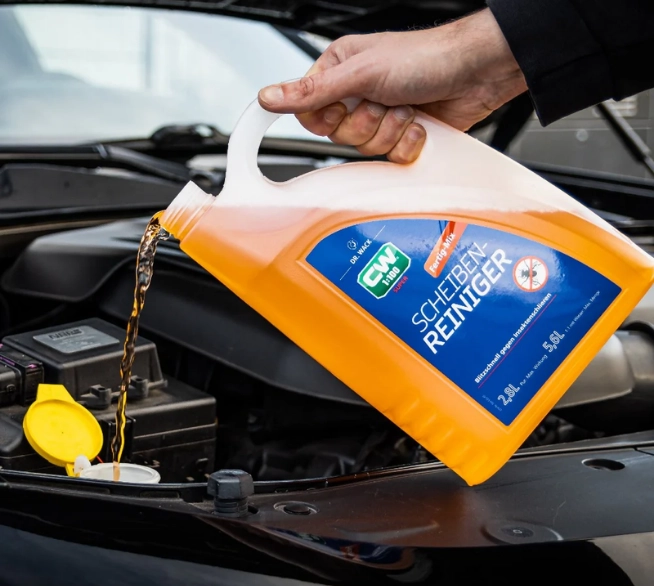 CW1:100 Super Scheibenreiniger wird aus einem 5-Liter-Kanister in den Behälter der Scheibenwaschanlage eines Autos gefüllt